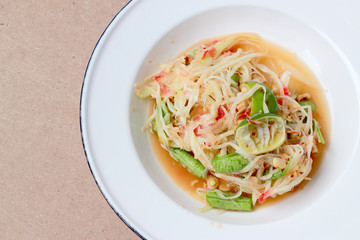 Green Papaya Salad (Som tum Thai) in white dish on wood table, Thai cuisine spicy delicious