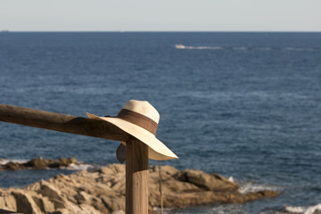 Fototapeta na wymiar Woman's hat on wood fence by the sea, beautiful view on sea and horizon