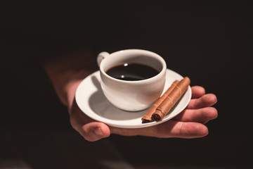 Male hands holding a cup of coffee over wooden table.