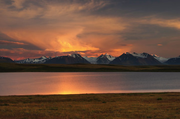 Highland dawn sunset lake on a background of snow ice covered high mountains and glaciers under cloudy colorful light illuminated dramatic sky, Plateau Ukok, Altai Siberia, Russia