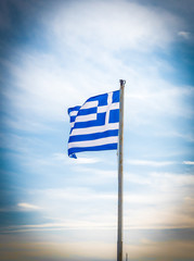 Greek flag waving in the wind in a blue sky and white clouds around .