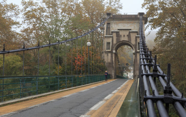 Fototapeta premium Man running over an old suspension bridge during a foggy, autumn day.