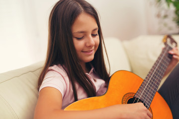Cute little girl practicing her guitar lessons at home
