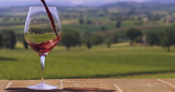 Slow motion macro still life of red wine poured in transparent glass isolated on scenic panoramic vineyard background (close up)