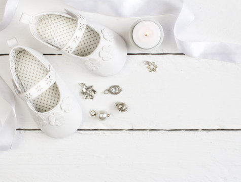 Overhead photo of pair of white baby booties, candle, ribbon and silver and crystal charms - Powered by Adobe