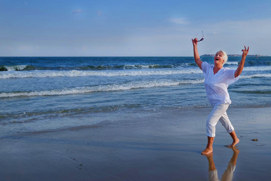 attractive senior grey haired woman dancing near sea shore. a woman dressed in a white blouse decorated with three rows of frills - Powered by Adobe