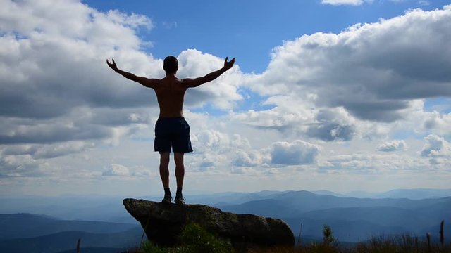 man stands on top of a mountain with open hands. 