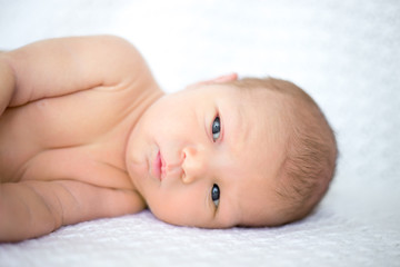 Close-up portrait of sweet newborn infant lying quietly on white bed serious looking away