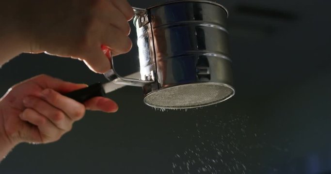 Super slow motion macro of a middle aged man baker sprinkling white sugar powder on a cake (close up)