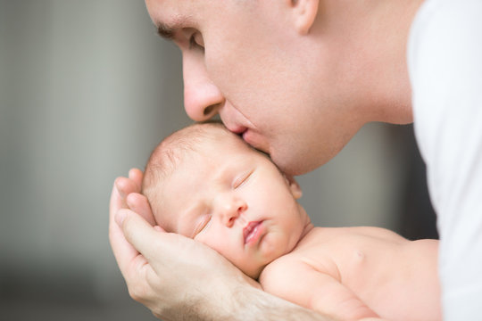 Young man kissing a newborn, he holds gently in his palms. Family, healthy birth concept photo, close up, horizontal