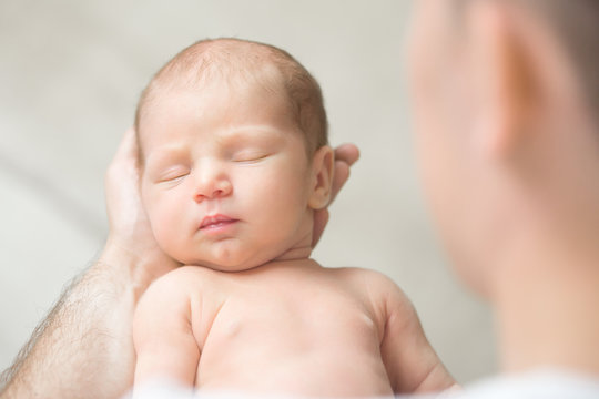 Portrait of a newborn hold in father palms, eyes closed. Family, healthy birth concept photo. View over the shoulder