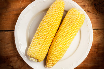 Maíz mazorca sobre un plato blanco redondo sobre una mesa de madera rústica. Vsita superior y de cerca