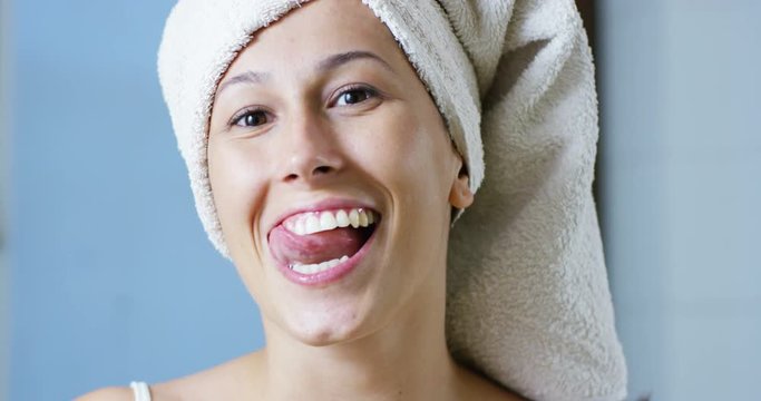 A girl over the shower brushing teeth with a toothbrush and toothpaste because it keeps us clean his mouth and wants to have white teeth and the 'fresh breath. smiles and passes his tongue between his