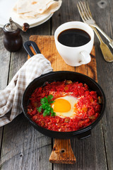Shakshuka with tomato sauce and fried egg in a cast iron pan for breakfast on the old wooden background. Rustic Style, Selective Focus.