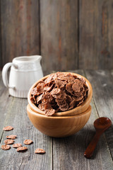 Chocolate cornflakes for breakfast in a bamboo plate on old wooden background. Selective focus.
