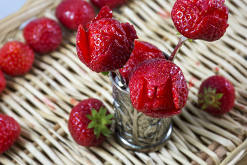 Red strawberries as flowers are in the metallic glass on the wicker background