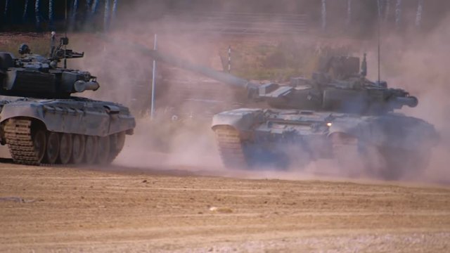 T-90 tanks are driving in a row on a ground road, stir up dust. Includes audio. Contains audio
