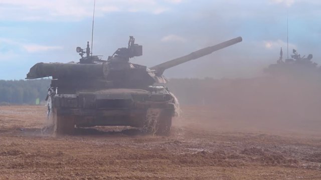 T-90 tanks are driving in a row on a ground road, stir up dust. Last machine has overcome the water barrier, water dripping from the armor. Includes audio. Contains audio