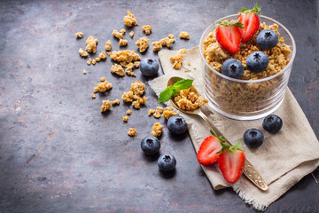Homemade muesli granola in glass with berries on rusty table