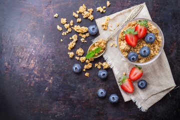 Homemade muesli granola in glass with berries on rusty table