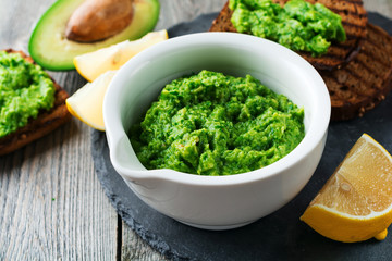 Traditional  mexican sauce guacamole in ceramic white bowl, lemon and cut half avocado on dark background. Selective focus.