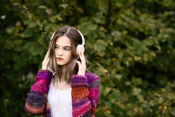 Woman in woolen sweater listening to music in park