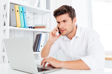 Handsome businessman using laptop computer and talking on the phone