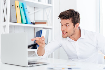 Angry annoyed businessman pointing finger at laptop