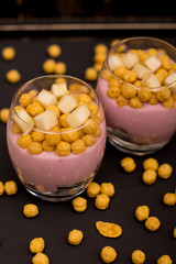Yogurt desserts with muesli and slices of apple on dark wooden background