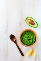 Traditional  mexican sauce guacamole in bamboo bowl, lemon and cut half avocado on white wooden background. Selective focus. Text place.