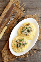 Homemade pasta with mushrooms, cheese and dill on a plate, fork, knife on old wooden background. Stuffed pasta nests recipe. Top view