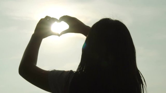 Woman shapes heart with hands over sun on sunset, Slow motion
