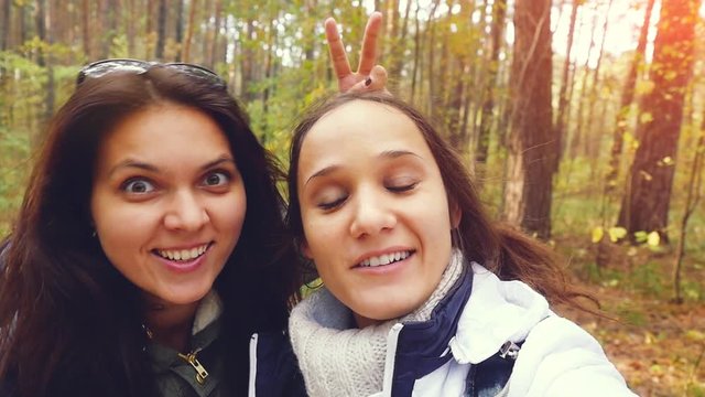 Two beautiful girls with cell phone camera taking photos in autumn fall park in slow motion. 1920x1080