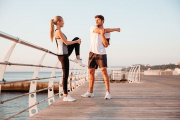 Young man and beautiful woman doing stretching exercises outdoors