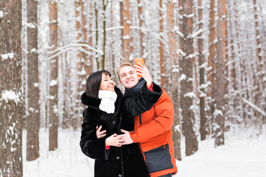 people, season, love, technology and leisure concept - happy couple taking picture with smartphone on over winter background
