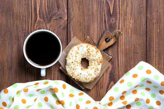 Donut with nuts and cup of coffee, wooden background, top view