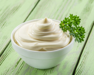 Natural mayonnaise in the white bowl on the wooden table.