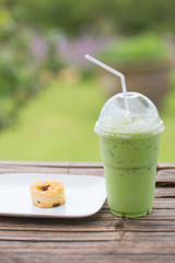 Iced milk green tea in plastic cup with lid and white straw on bamboo table in nature