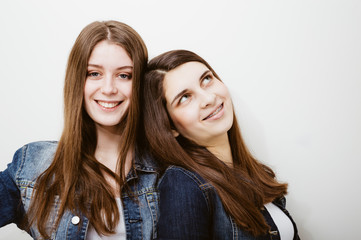fashion photo of two beautiful young women with long dark hair and bright makeup wears casual clothes,posing in studio