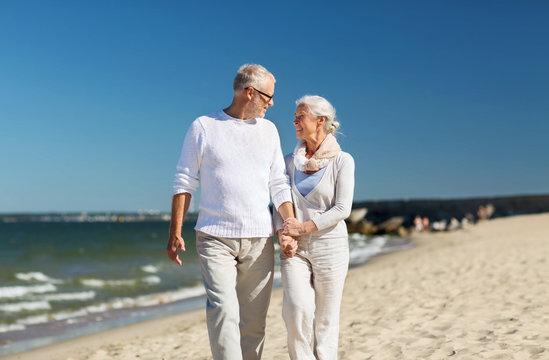 happy senior couple holding hands on summer beach