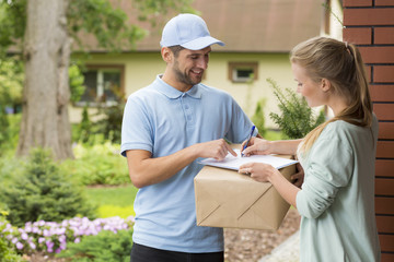 Courier holding a parcel and woman signing a delivery form - obrazy, fototapety, plakaty