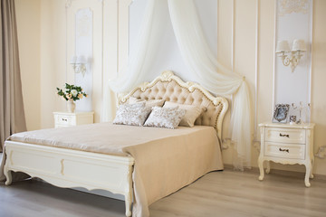 Bedroom in soft light colors. Big comfortable double bed in elegant classic interior