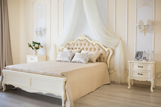 Bedroom in soft light colors. Big comfortable double bed in elegant classic interior