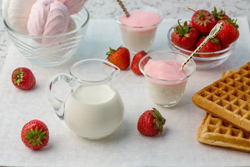 Food. On a white background, yoghurt, biscuits, milk, marshmallows, cookies, cheese, strawberry. In a glass container. Strawberries scattered on the table.