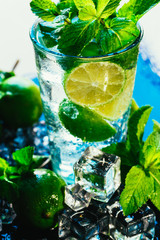 glass of mojito with lime and mint ice cube close-up red straw on blue background