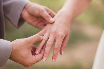 Obraz na płótnie Canvas Closeup of a groom putting a gold wedding ring onto the bride's finger