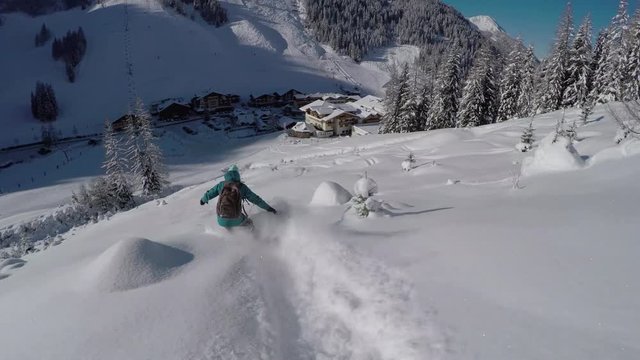 Female snowboarder riding fresh powder snow towards idyllic Austrian town resort