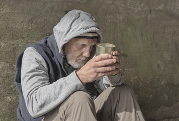 Portrait image of a mature homeless man sitting outdoors with a tin can