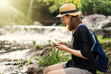 Pretty woman is using smartphone resting at the waterfall in a forest