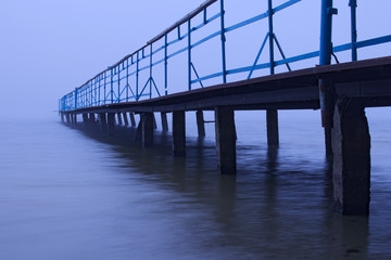 Misty morning on the lake. Old abandoned pier goes into the fog